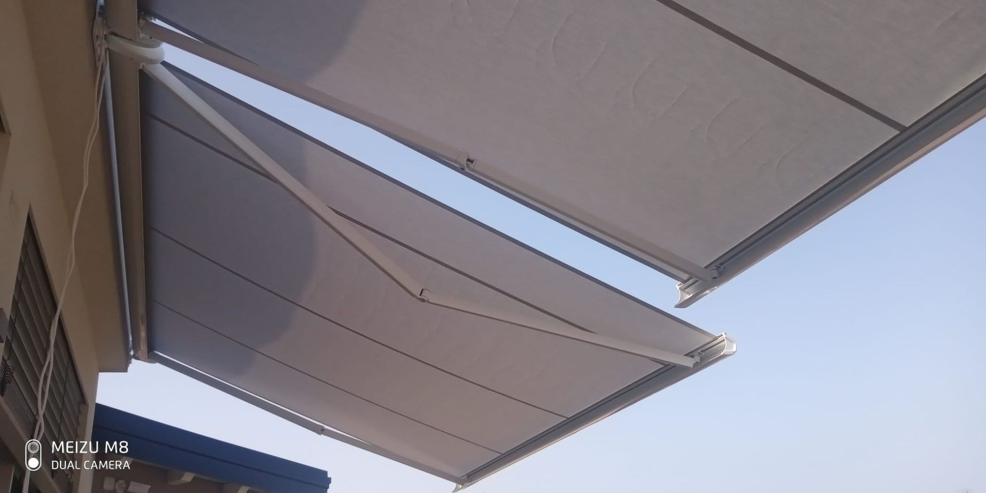 Tende da sole retrattili che si estendono sulla facciata di un edificio, illuminate dal sole, stagliano un cielo azzurro.