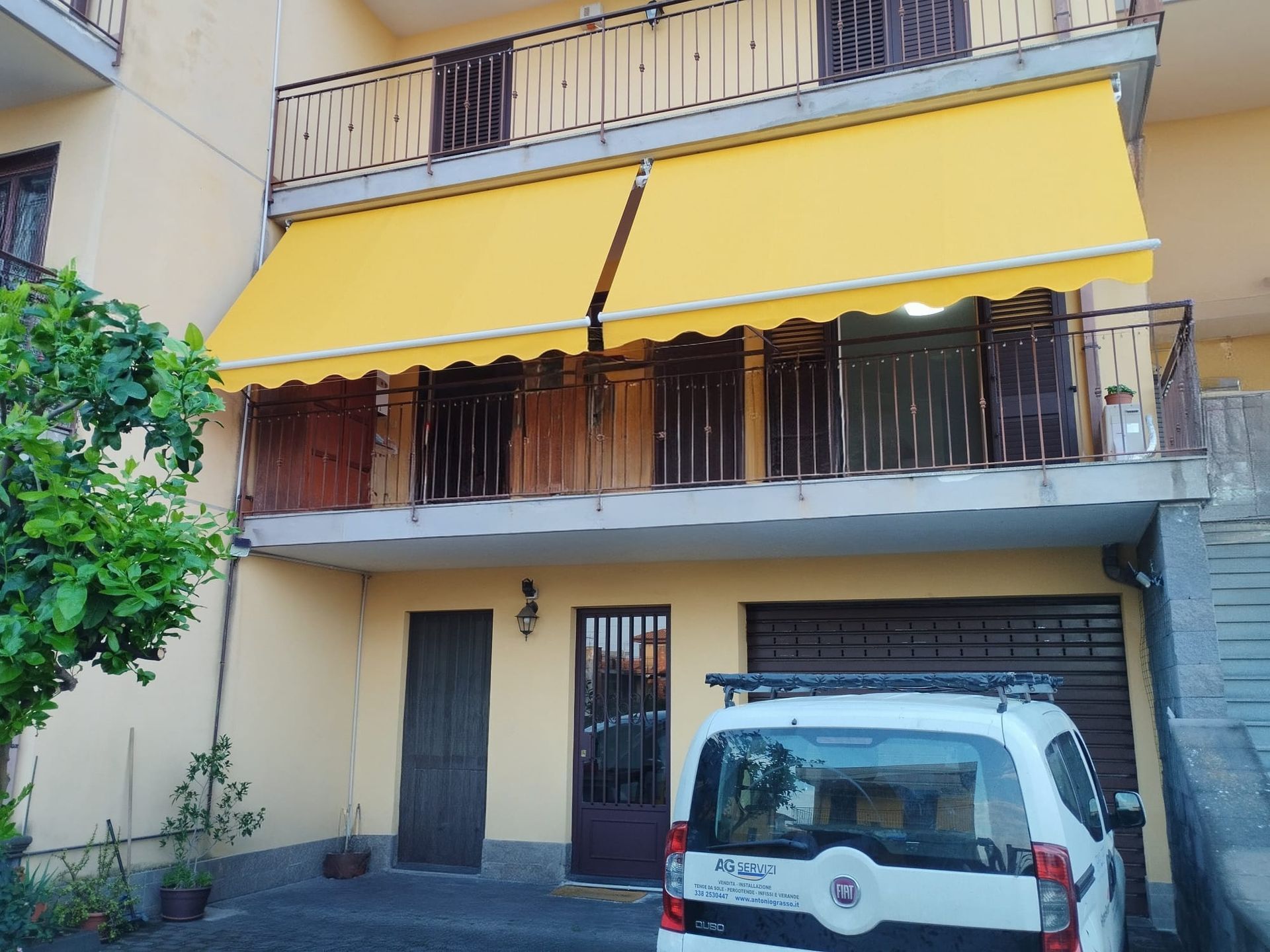 Palazzo di appartamenti con tende da sole gialle e un furgone bianco parcheggiato davanti.