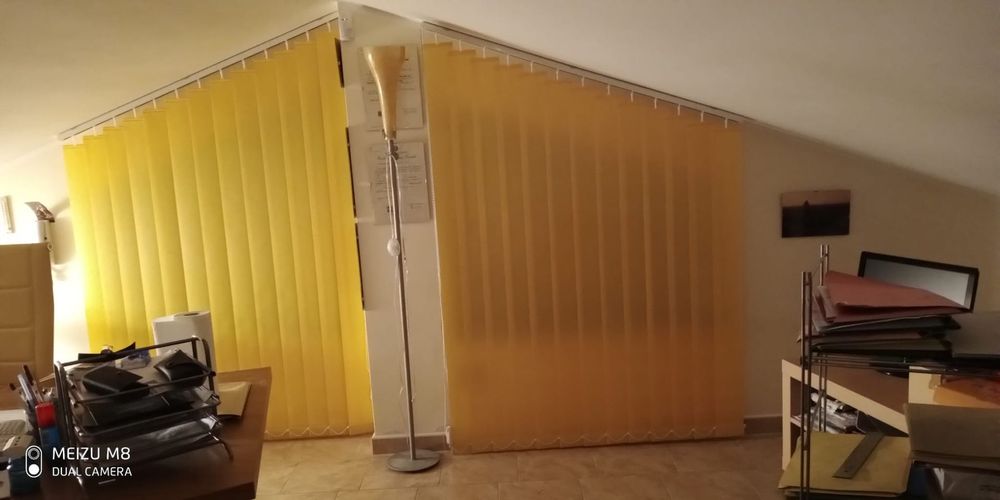 Tende a rullo gialle in una stanza con scrivania, scaffali e soffitto inclinato.