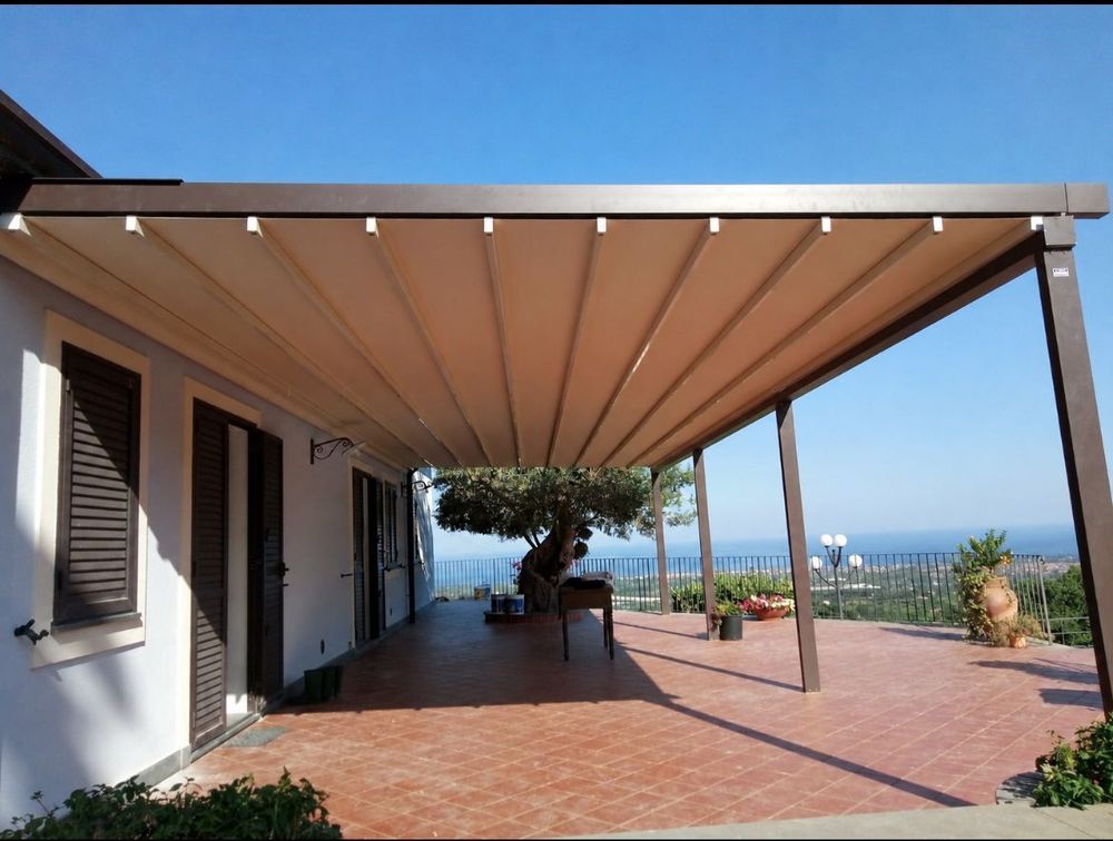 Pergola in legno su una terrazza soleggiata con porte scorrevoli in vetro e piante in vaso.