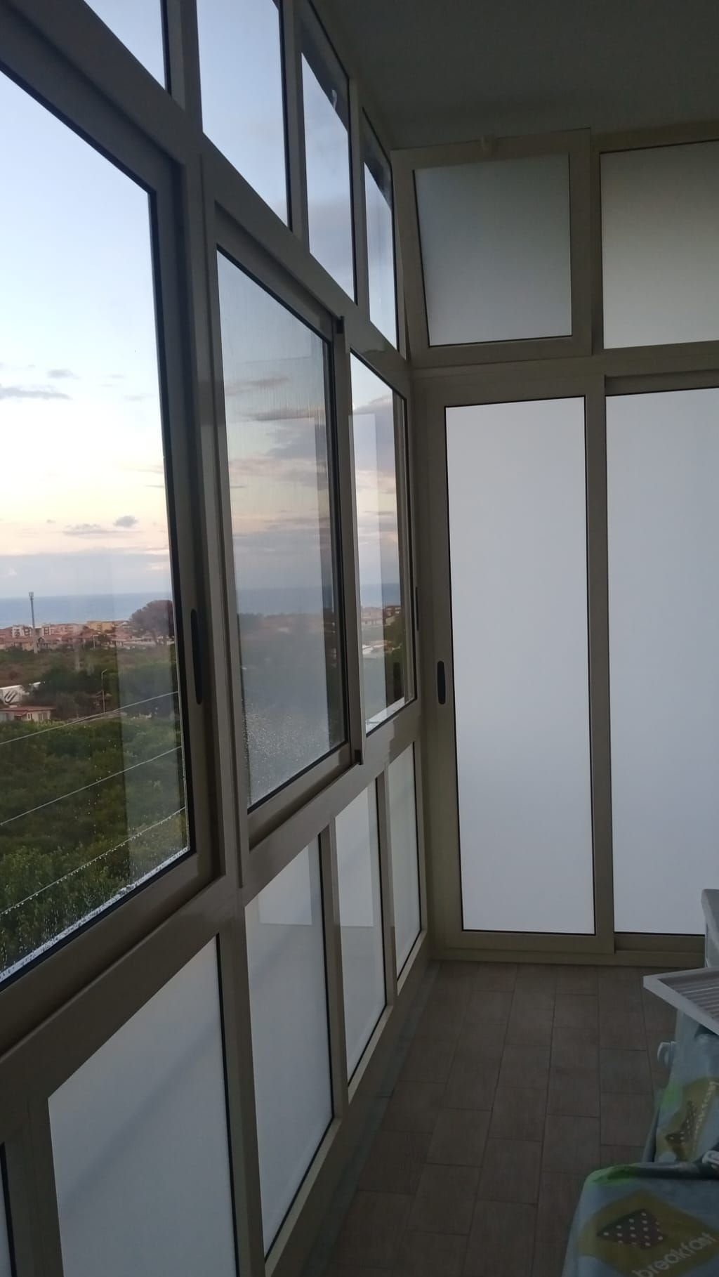 Tavolini da caffè all'aperto in un patio bianco con vetrate, accanto a un edificio arancione con piante in vaso.