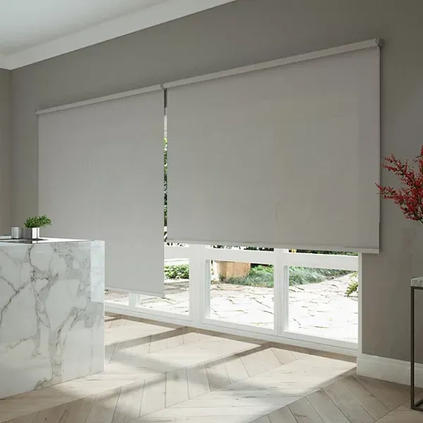 Stanza moderna con tende a rullo bianche che coprono ampie finestre, luce naturale soffusa e un bancone in marmo in primo piano.