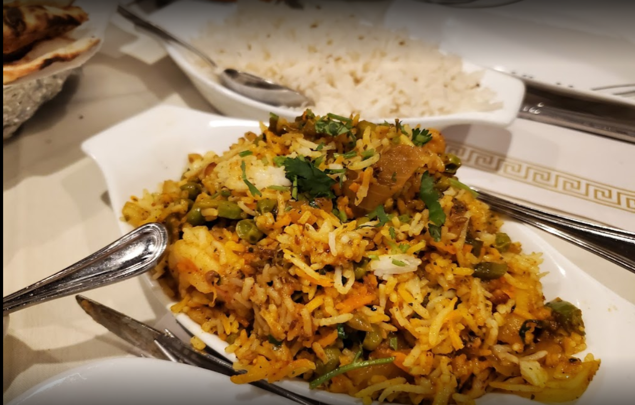 A colorful plate of biryani rice with peas and herbs, with a side of white rice.
