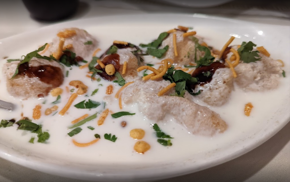 Dahi Vada: Deep-fried lentil dumplings in yogurt, garnished with chutney, sev, and cilantro.