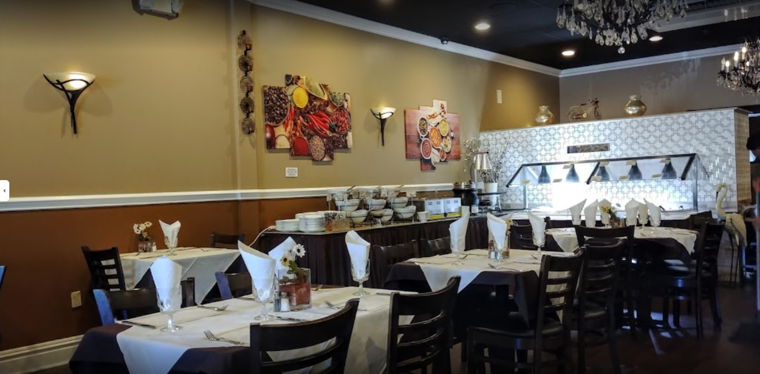 Interior of a restaurant with tables set for dining and a buffet area. Brown and white color scheme.
