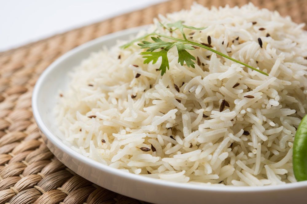 Plate of fluffy white rice with cumin seeds and cilantro garnish.