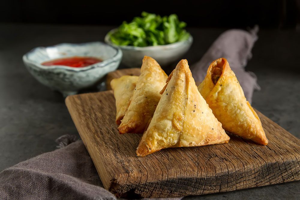 Golden samosas on a wooden board with small bowls of sauce and lettuce.