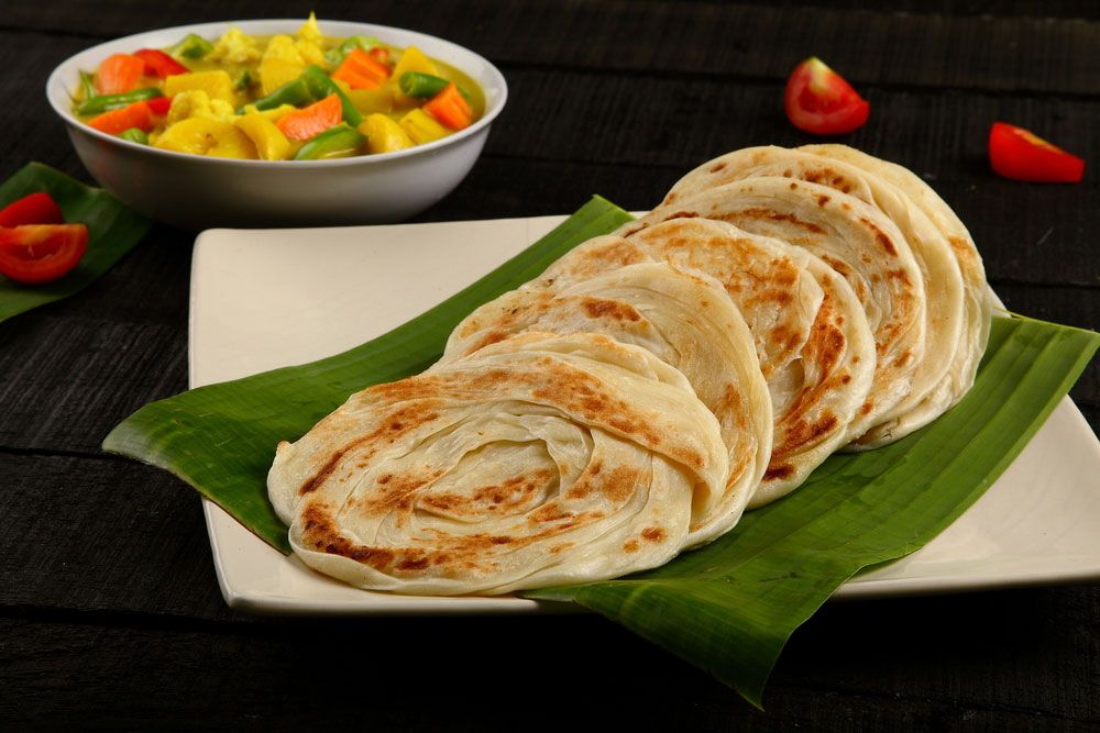 Parotta bread with a vegetable curry, served on a white plate with a banana leaf.