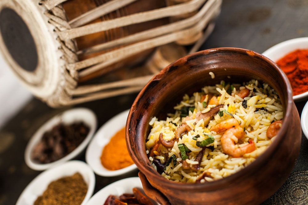 Clay pot of rice pilaf with shrimp, spices, and a tabla drum in the background.