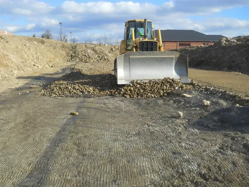 Bulldozer pushing gravel in a construction site with dirt piles and a building in the background