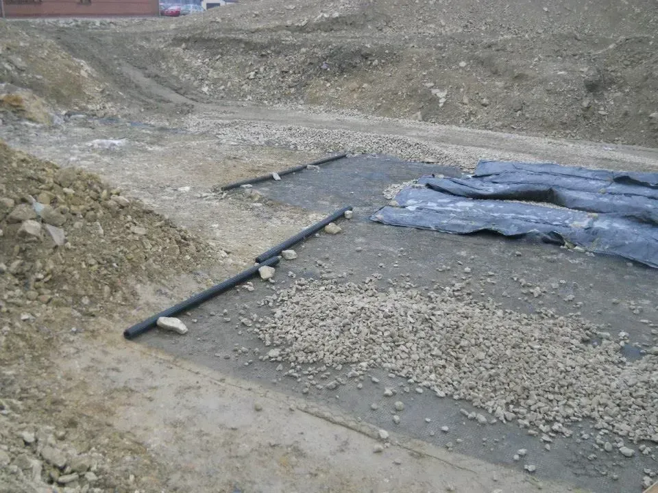 Construction site trench with black pipes, gravel, and tarps on dirt ground