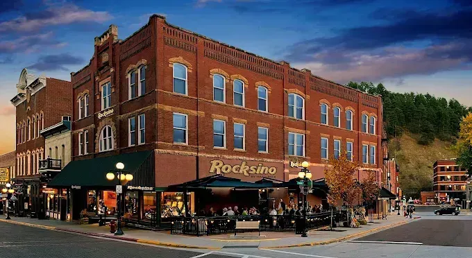 Historic red-brick corner building with a rooftop sign and lively street-level shops at dusk