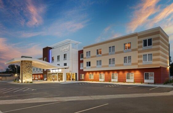 A modern hotel exterior with a tan, white, and red facade under a vibrant sunset sky, featuring a large stone entryway.