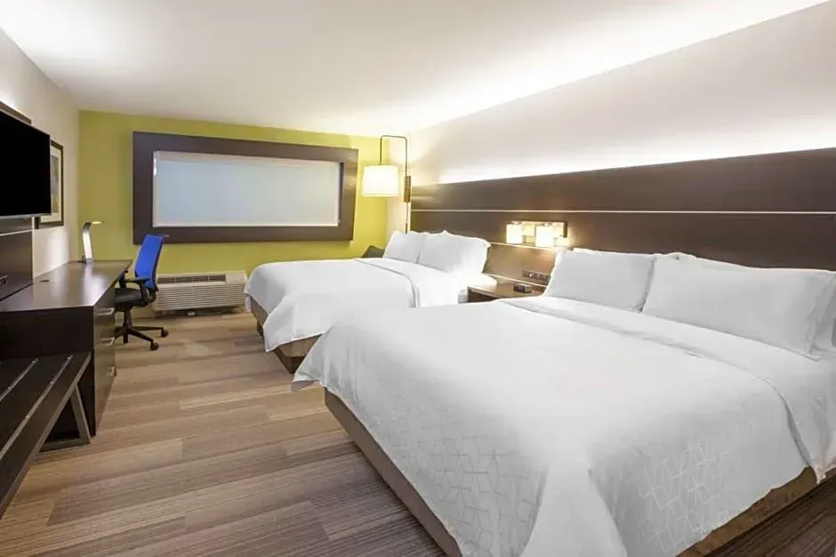 Hotel room with two white beds, desk, chair, lamp, and wall-mounted TV