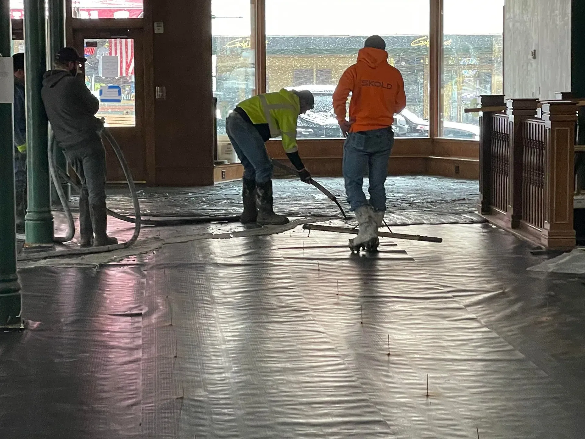 Workers mopping a wet indoor floor near large windows, with city view outside.