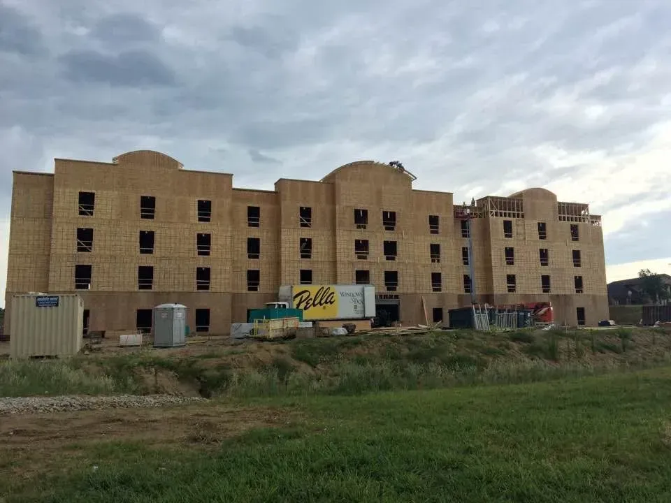 Abandoned beige apartment building with broken windows and grass in front under a cloudy sky