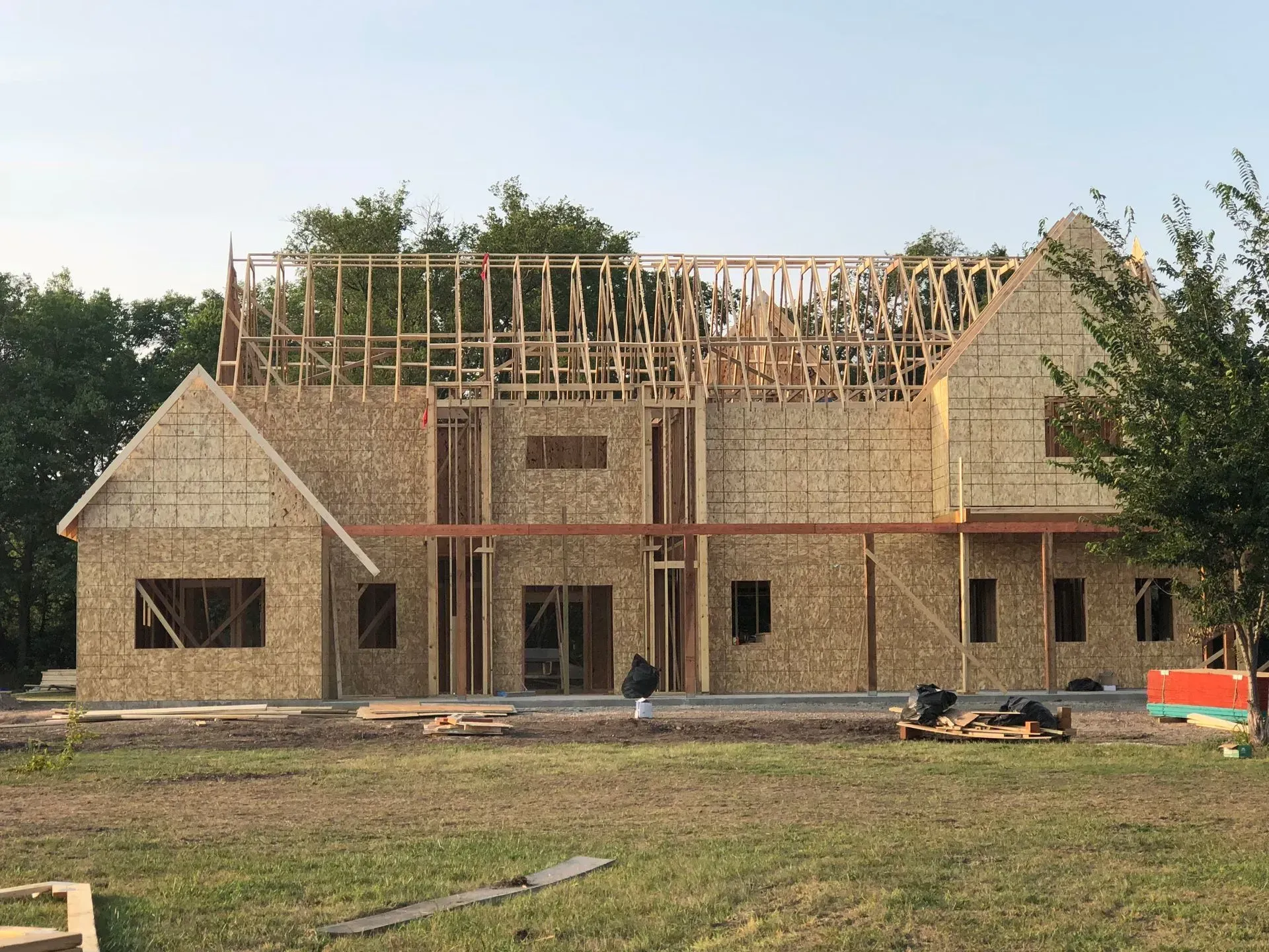 House under construction with exposed framing and brick exterior in a grassy lot