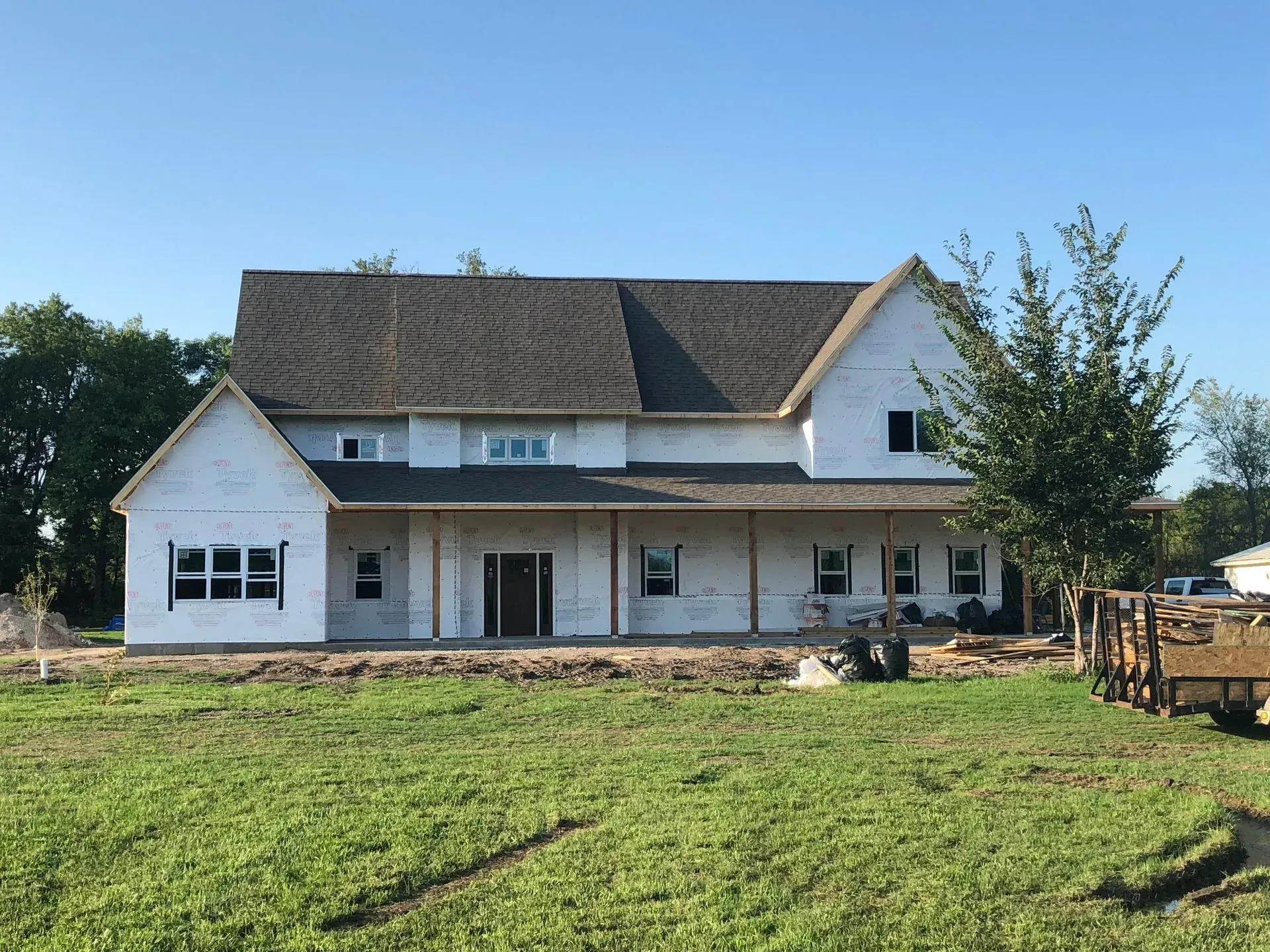 White farmhouse with gray roof and front porch behind a grassy yard under a clear sky