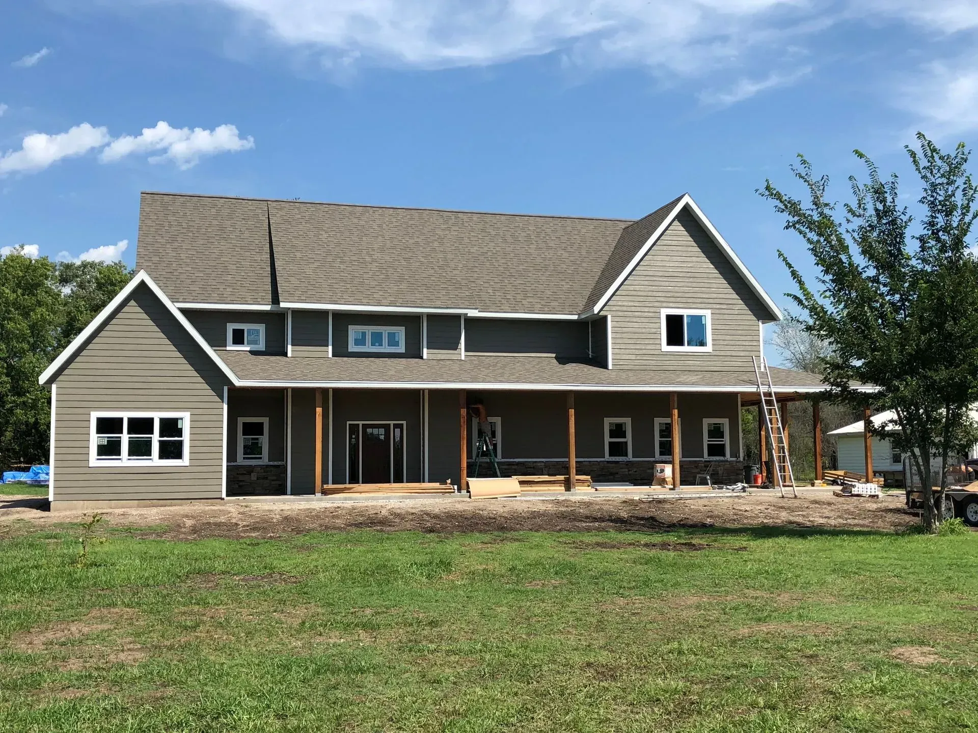New gray house with front porch and gabled roof in a grassy yard under a blue sky