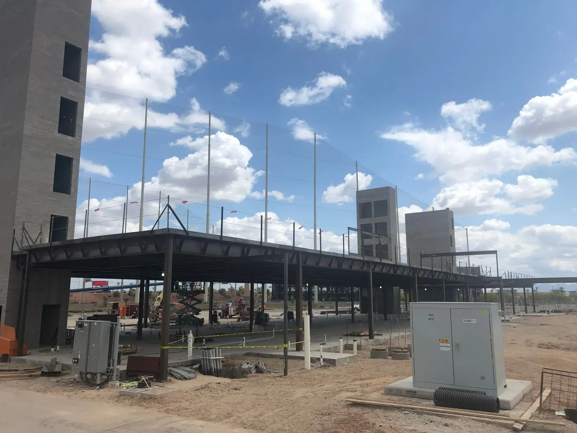 Elevated roadway under construction beside a tall building, with utility boxes and a cloudy sky