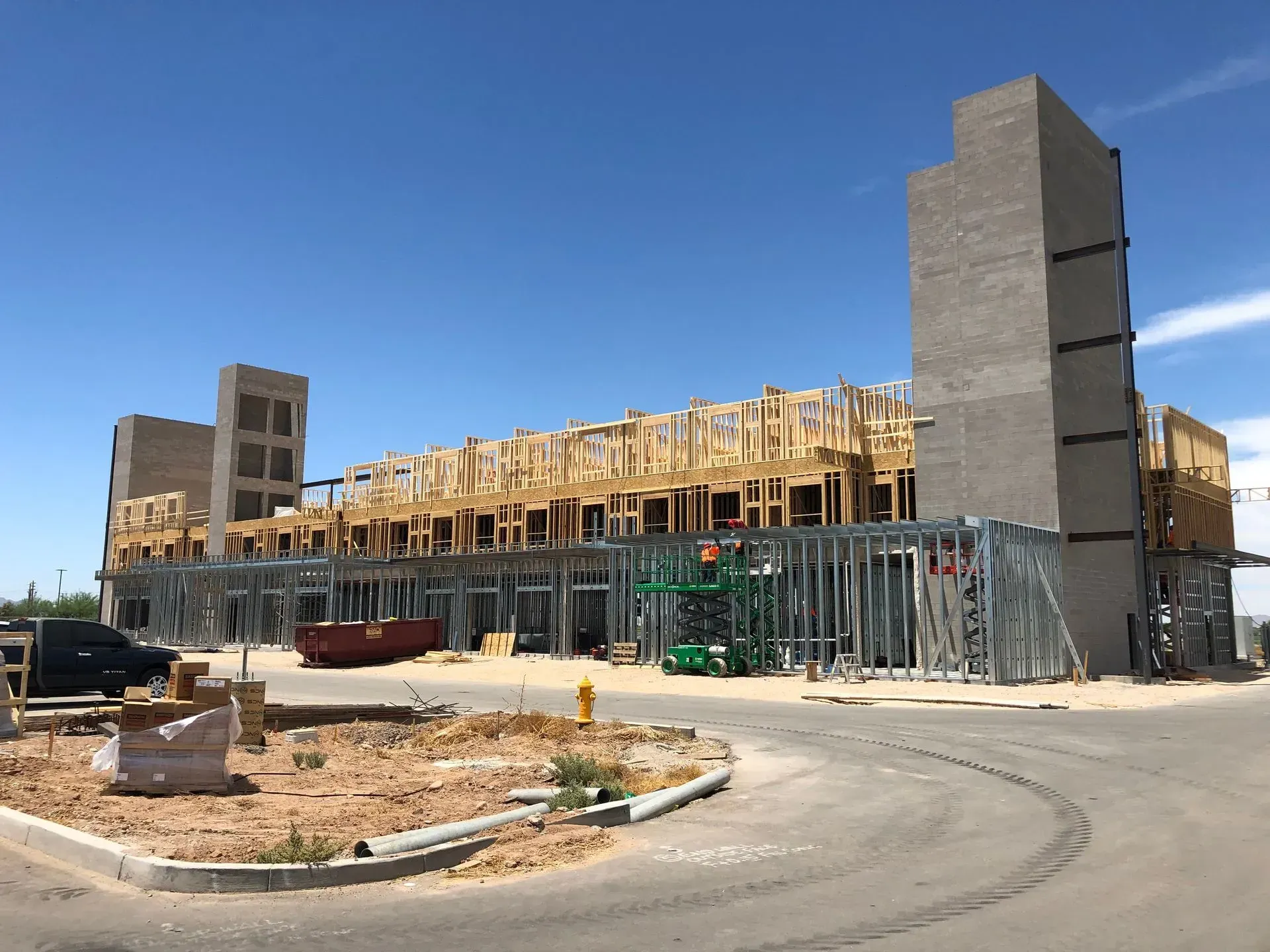 Construction site with concrete building frame, scaffolding, and a curved road under a clear blue sky