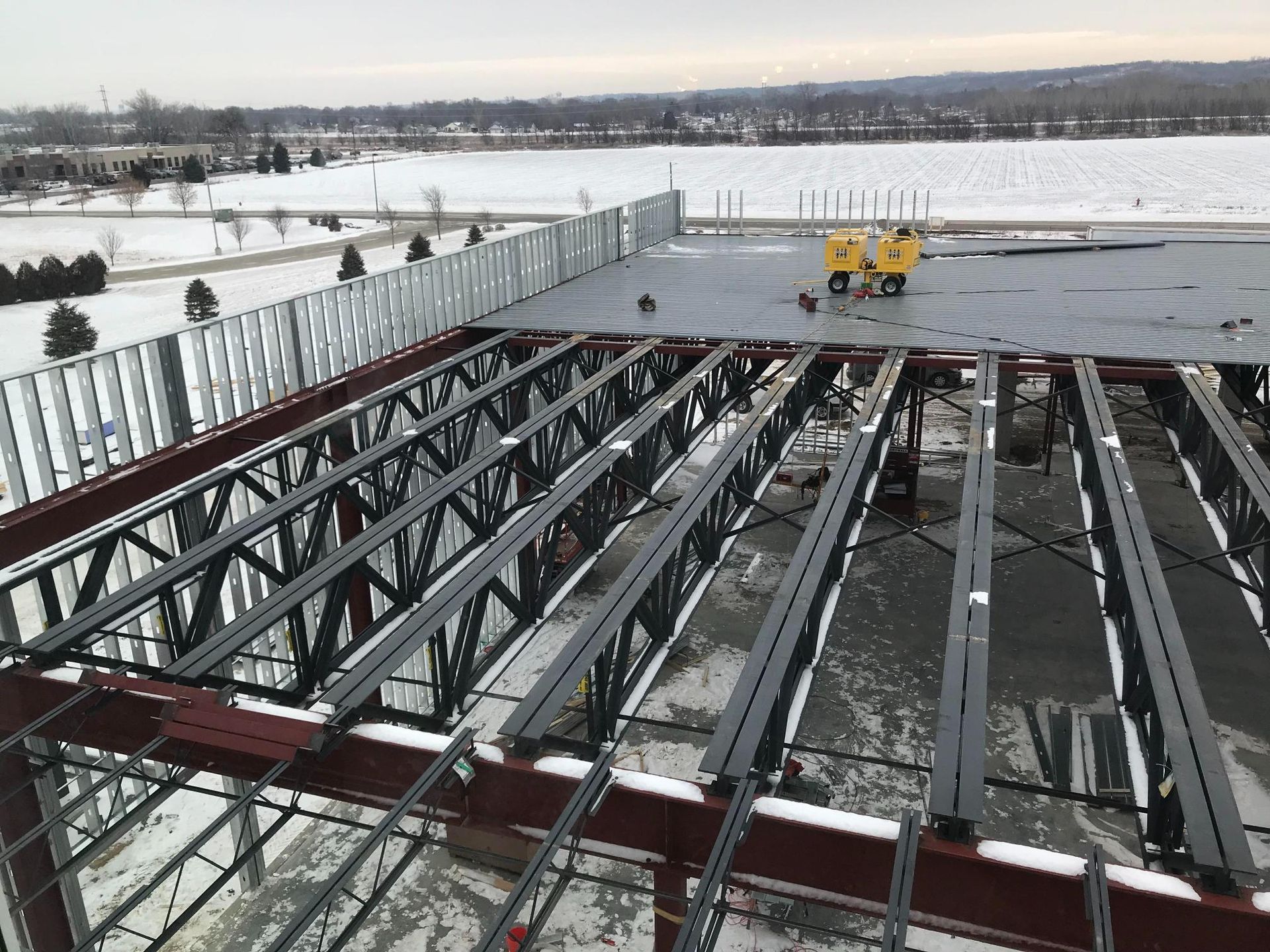 Snowy waterfront deck under construction with exposed steel beams and two yellow machines in the distance