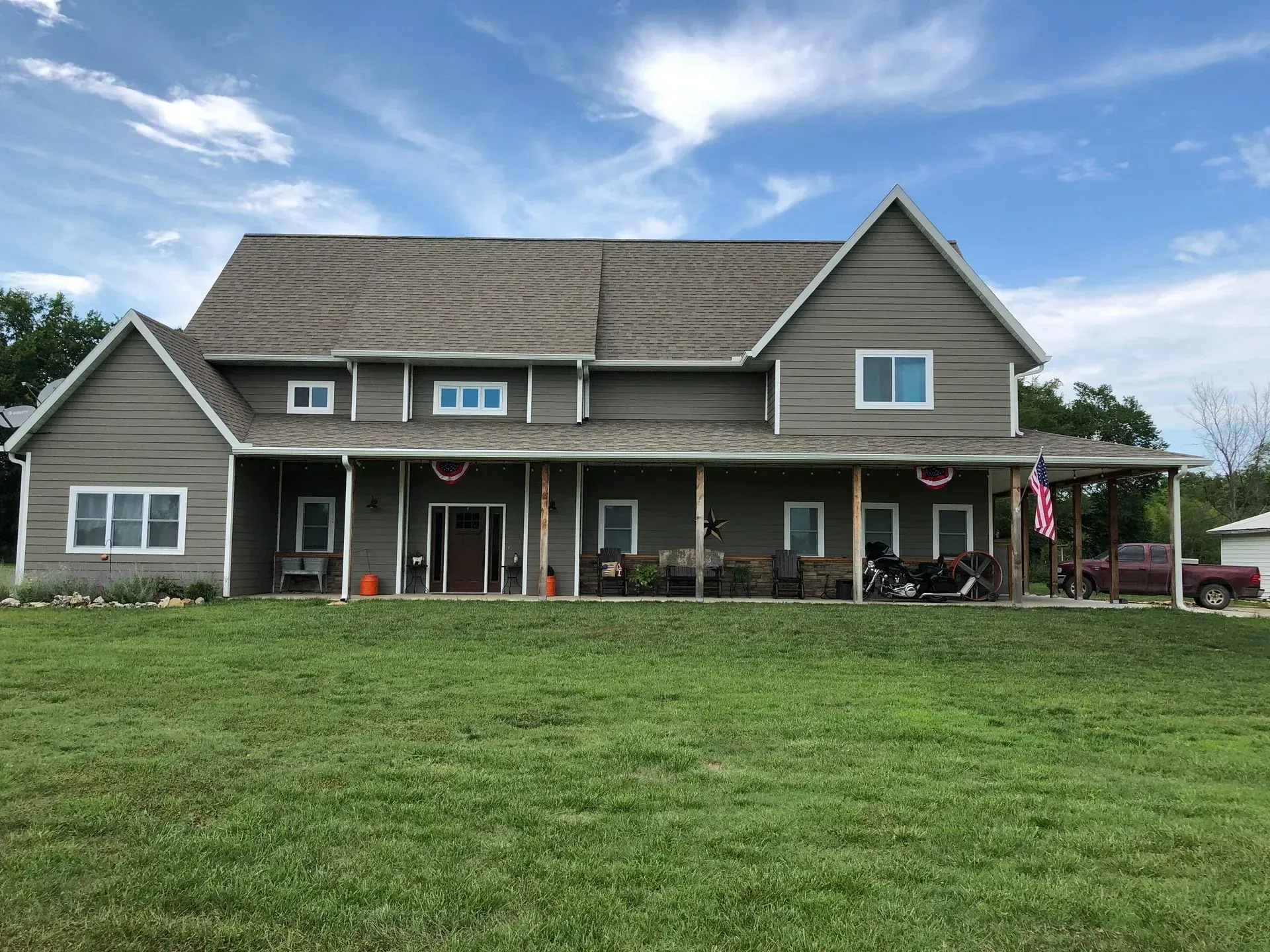 Large gray house with a covered porch and spacious green lawn under a partly cloudy sky