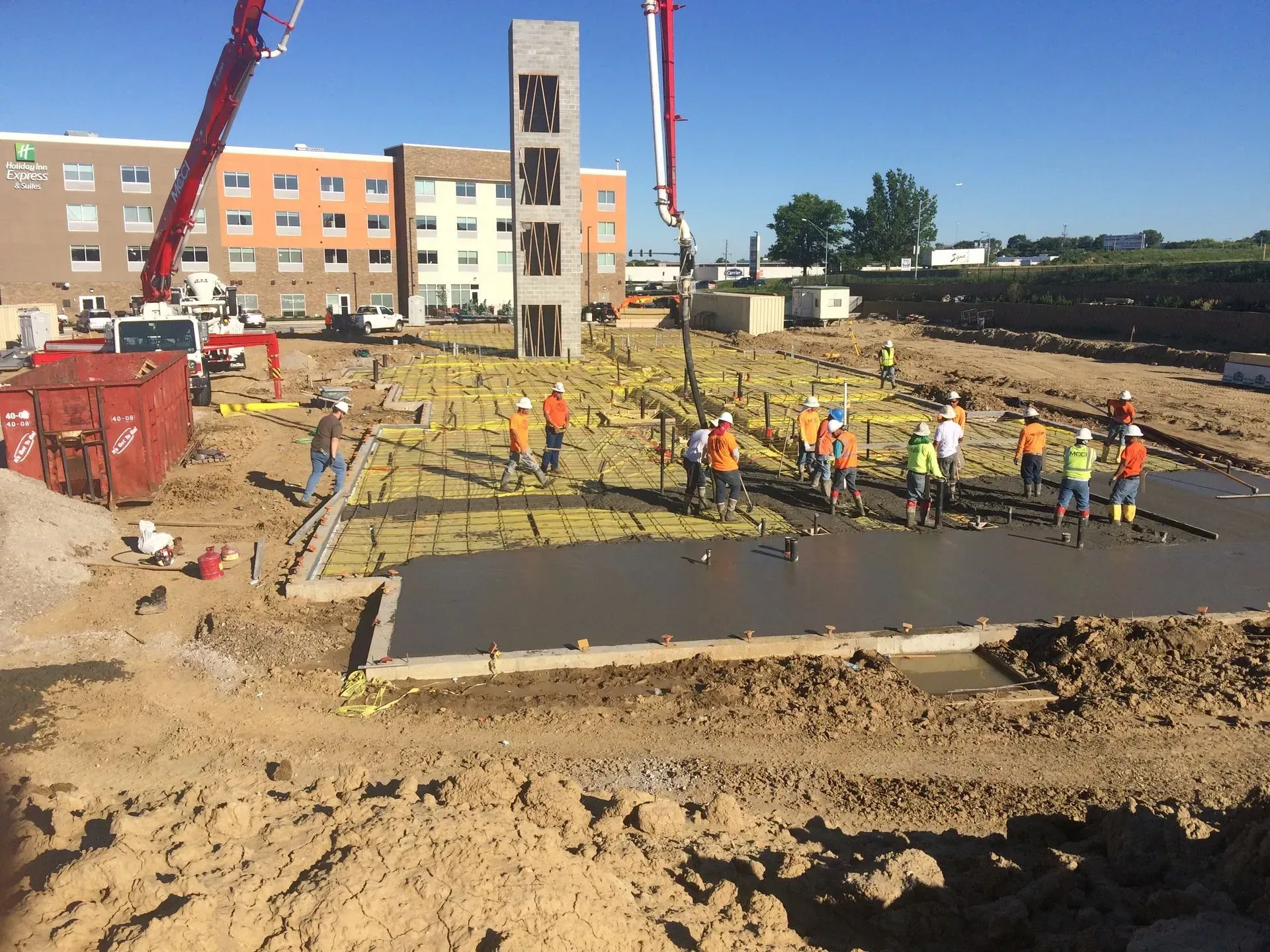 Construction site with workers pouring concrete foundation near a building and crane.