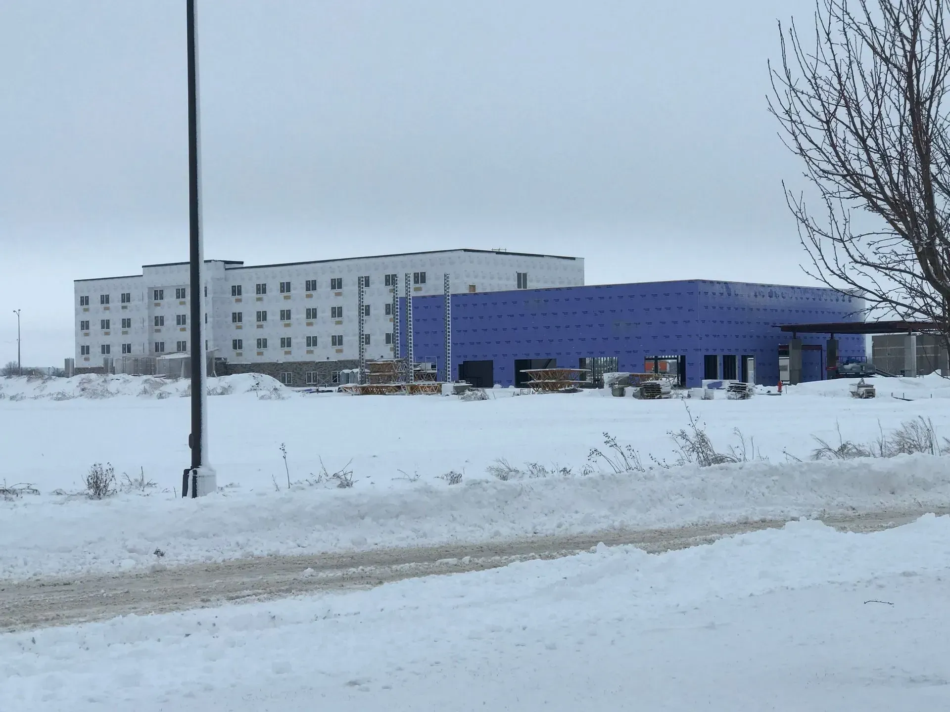 Snowy street with a gray building and a blue warehouse under an overcast sky