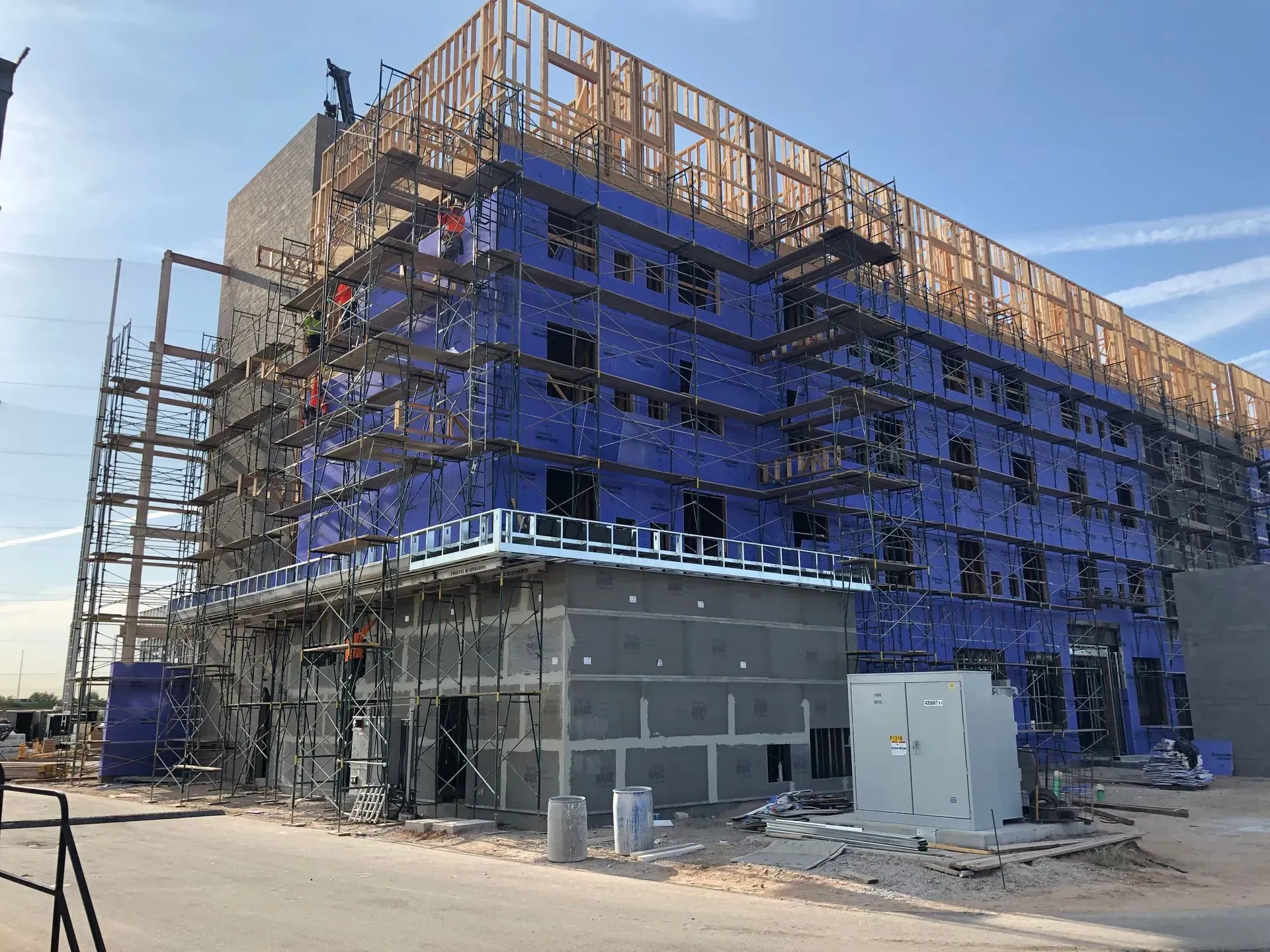 Partially built multi-story building wrapped in blue scaffolding at a construction site
