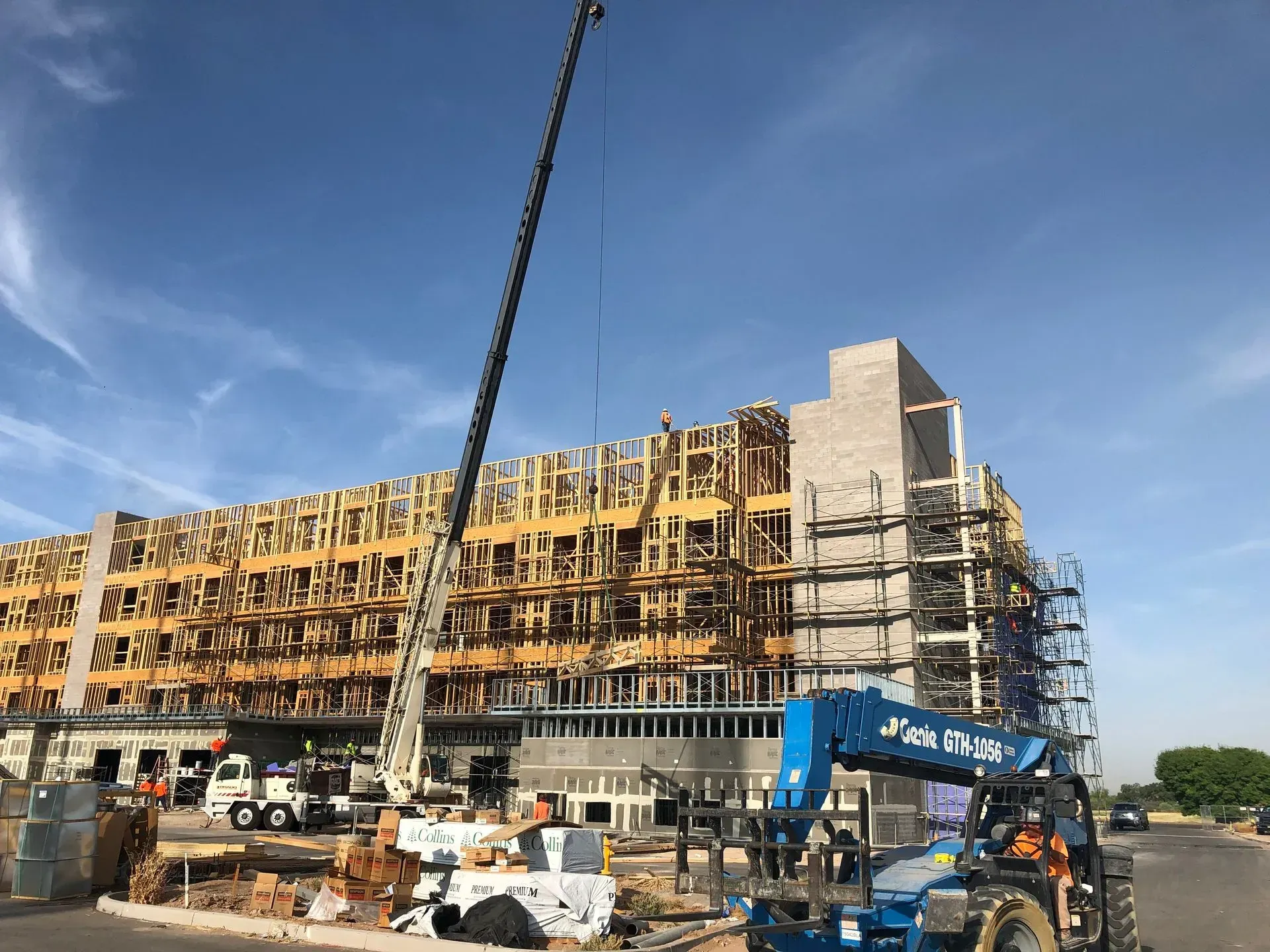 Construction site with a multi-story building under construction, cranes, and scaffolding against a blue sky