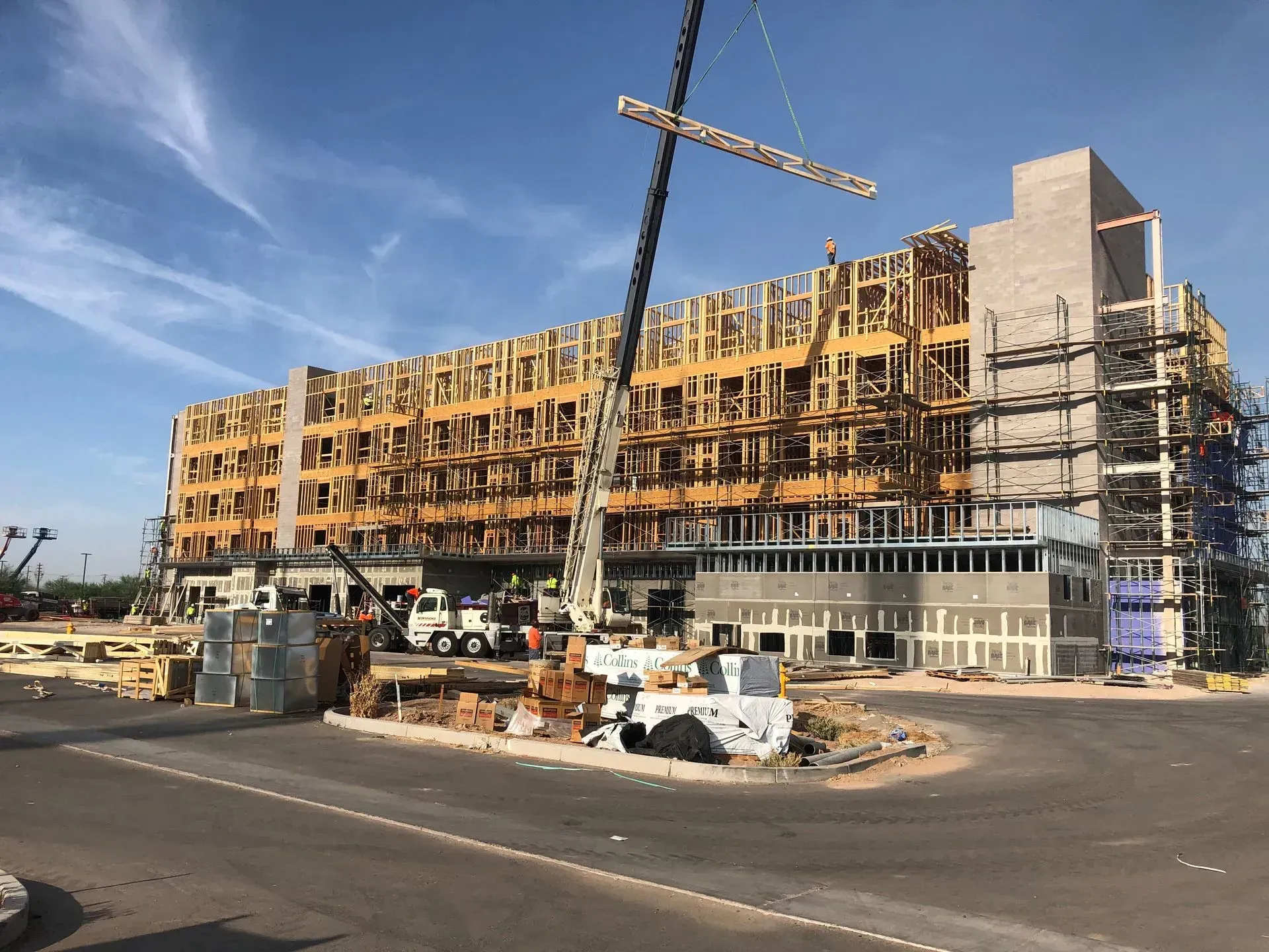 Construction site with a large building under renovation, scaffolding, and a crane beside a road