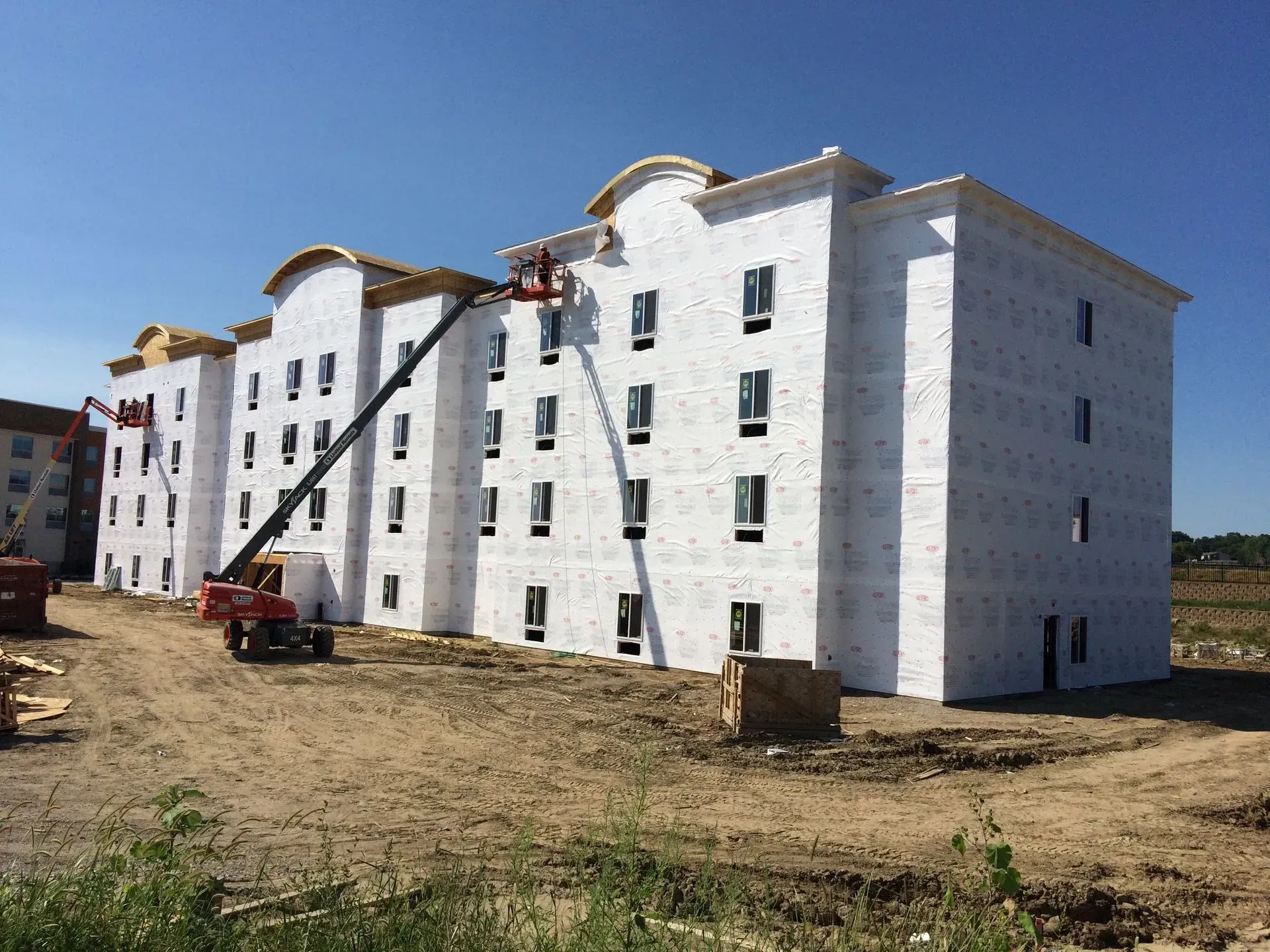 White multi-story apartment buildings under construction on a dirt lot with a red lift under a blue sky