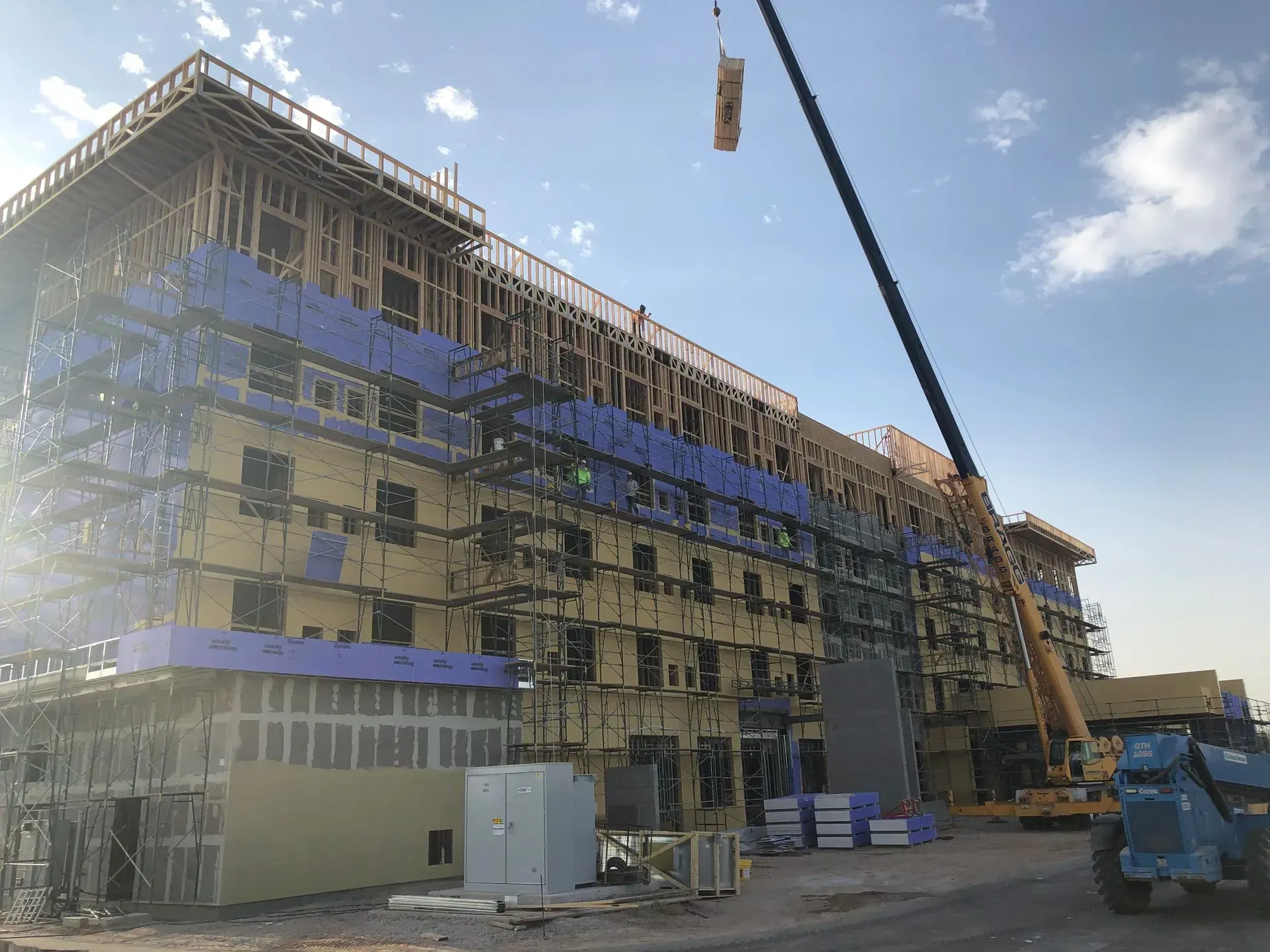 Multi-story building under construction with scaffolding, a crane, and blue sky.