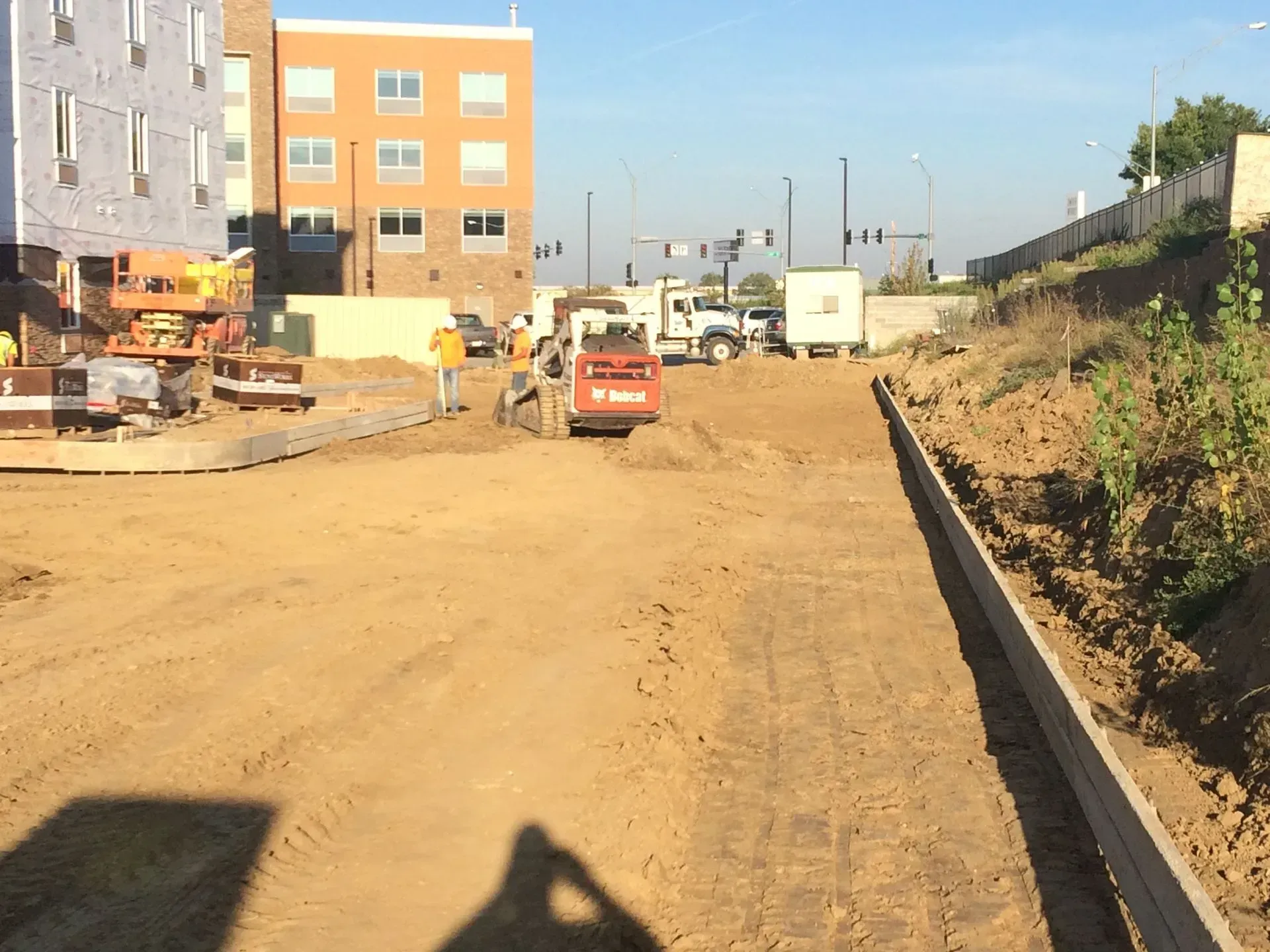 Construction site with dirt road, excavator, trucks, and partially built buildings under clear sky