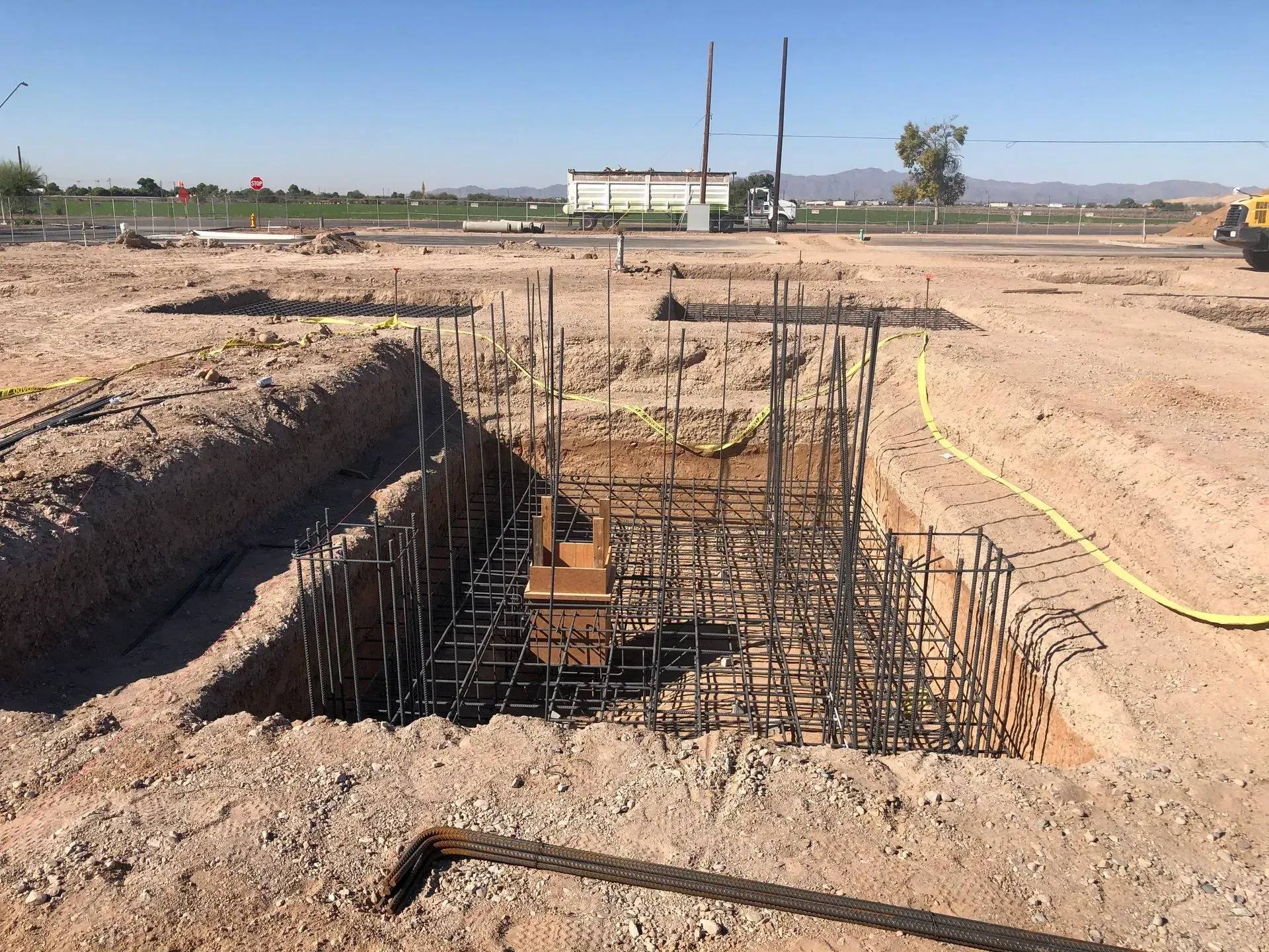 Construction site with an excavated foundation pit and exposed rebar under a clear sky