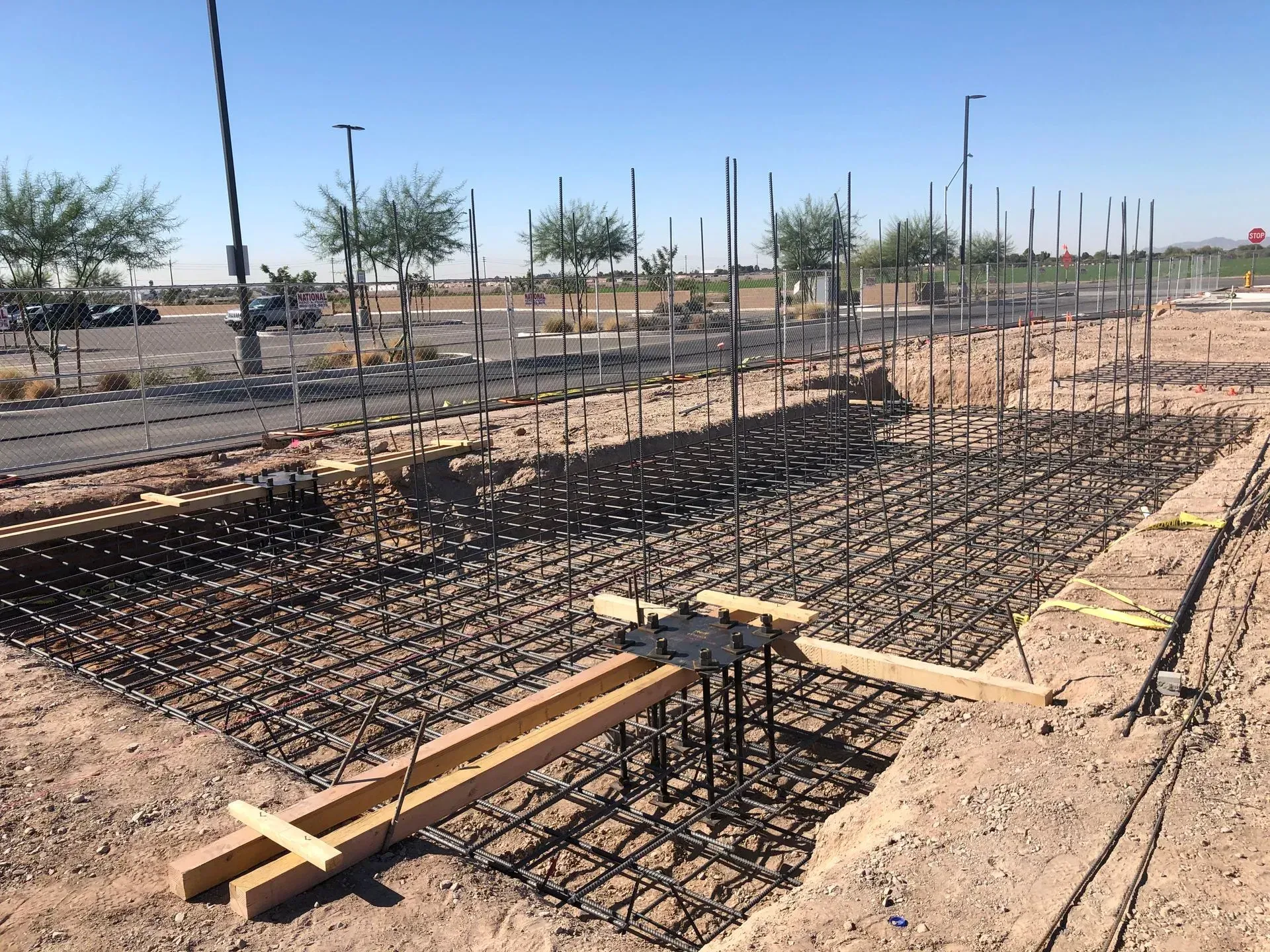 Rebar foundation grid at a construction site with wooden formwork and a paved road in the background
