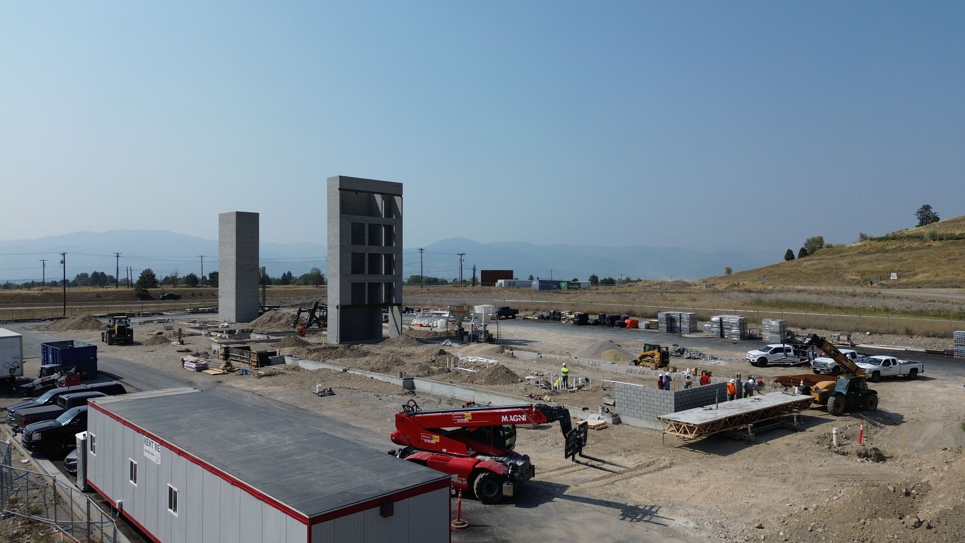 Construction site with concrete building frames, debris, and red machinery under a clear sky