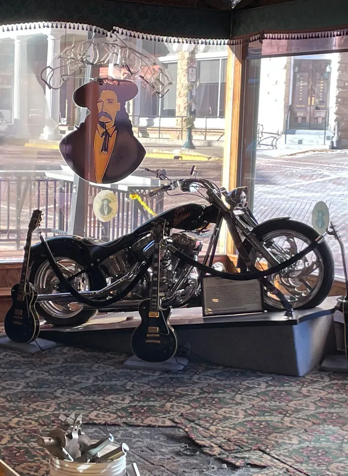 Black motorcycle on display indoors, with guitars and a guitar-shaped sign in the background.