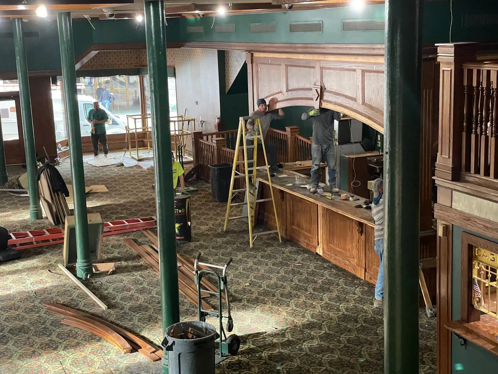 Indoor construction site with green support columns, a wood archway, and workers in the background