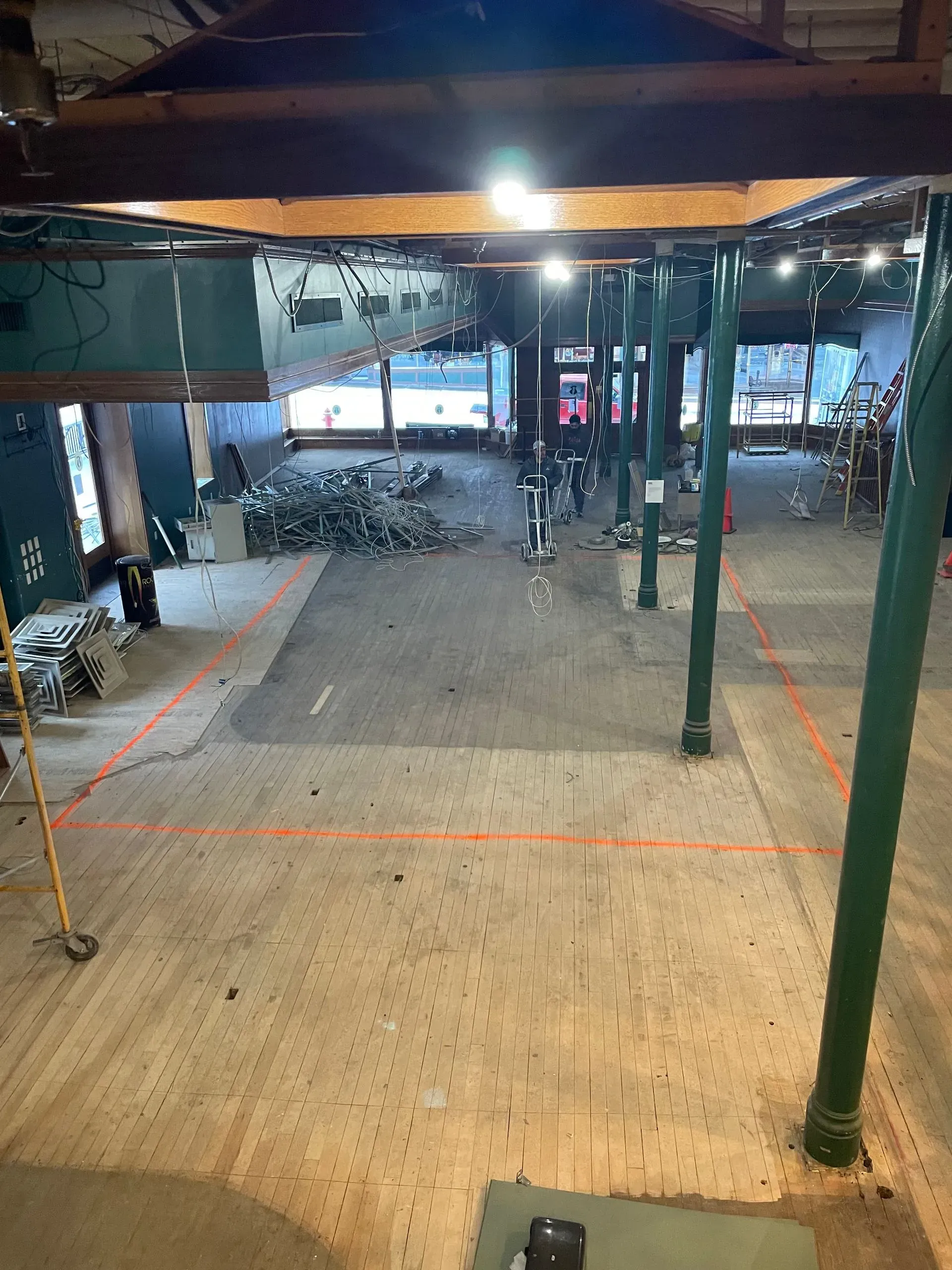 Covered outdoor walkway with green posts, a lit ceiling, and bicycles parked in the background.