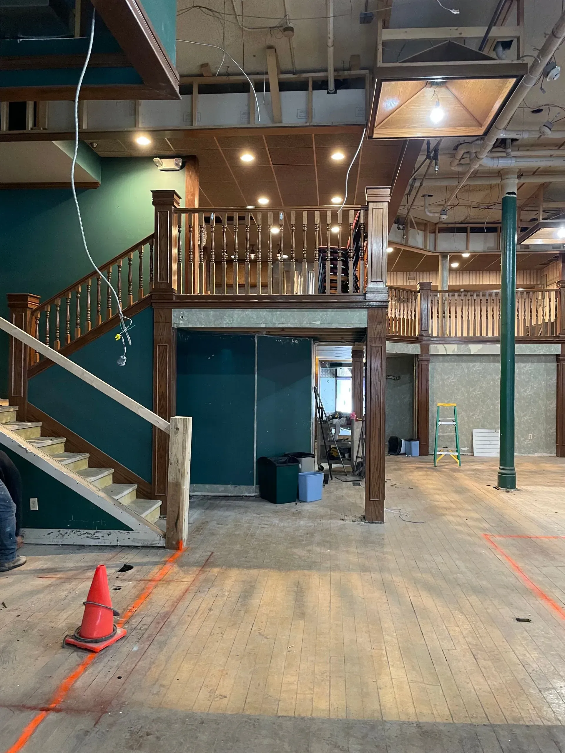 Indoor construction area with loft, wooden stairs, exposed ceiling, and orange cones on a concrete floor
