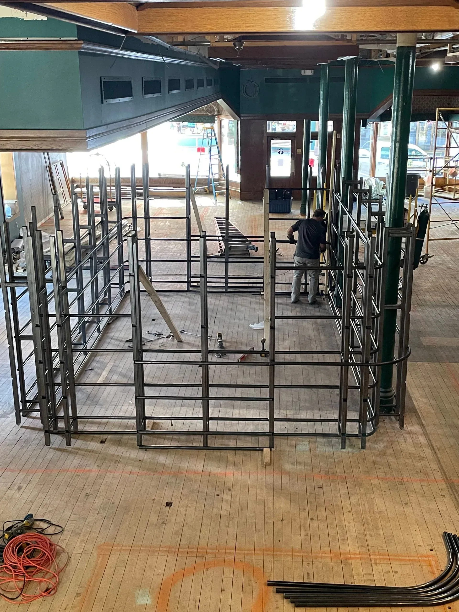Construction site with metal scaffolding and rails inside a partially built structure, with debris on the floor.