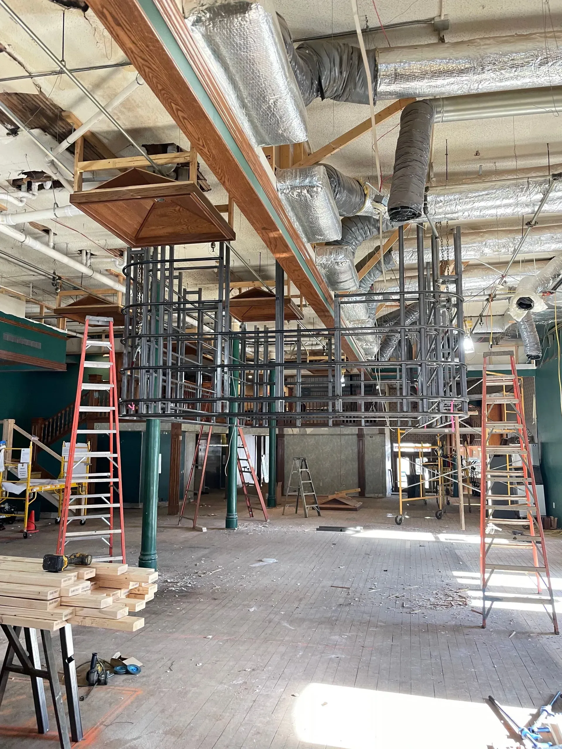 Indoor construction site with scaffolding, ladders, exposed ductwork, and building materials scattered on the floor