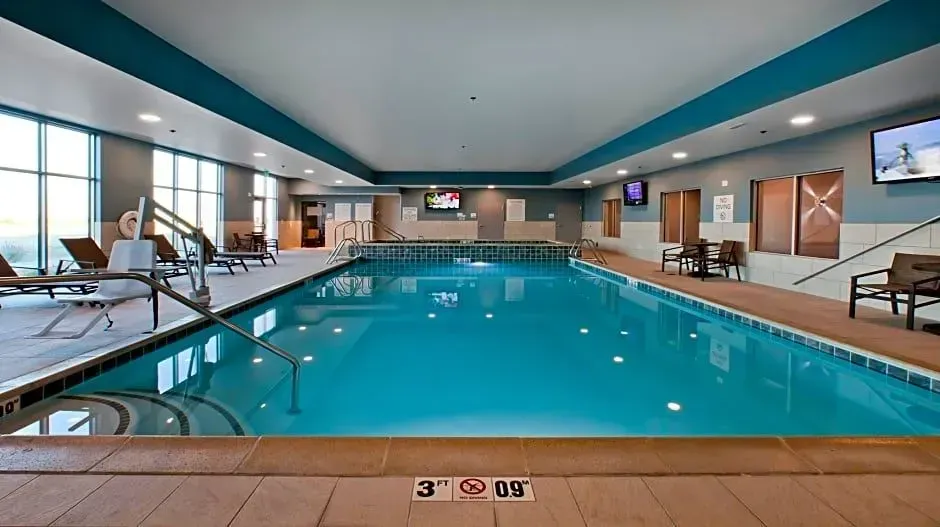 Indoor hotel swimming pool with clear blue water, lounge chairs, and large windows around the deck