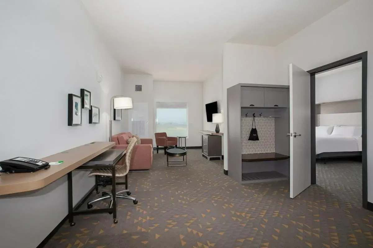 Hotel room with two beds, desk, chair, and open wardrobe in a bright, modern interior