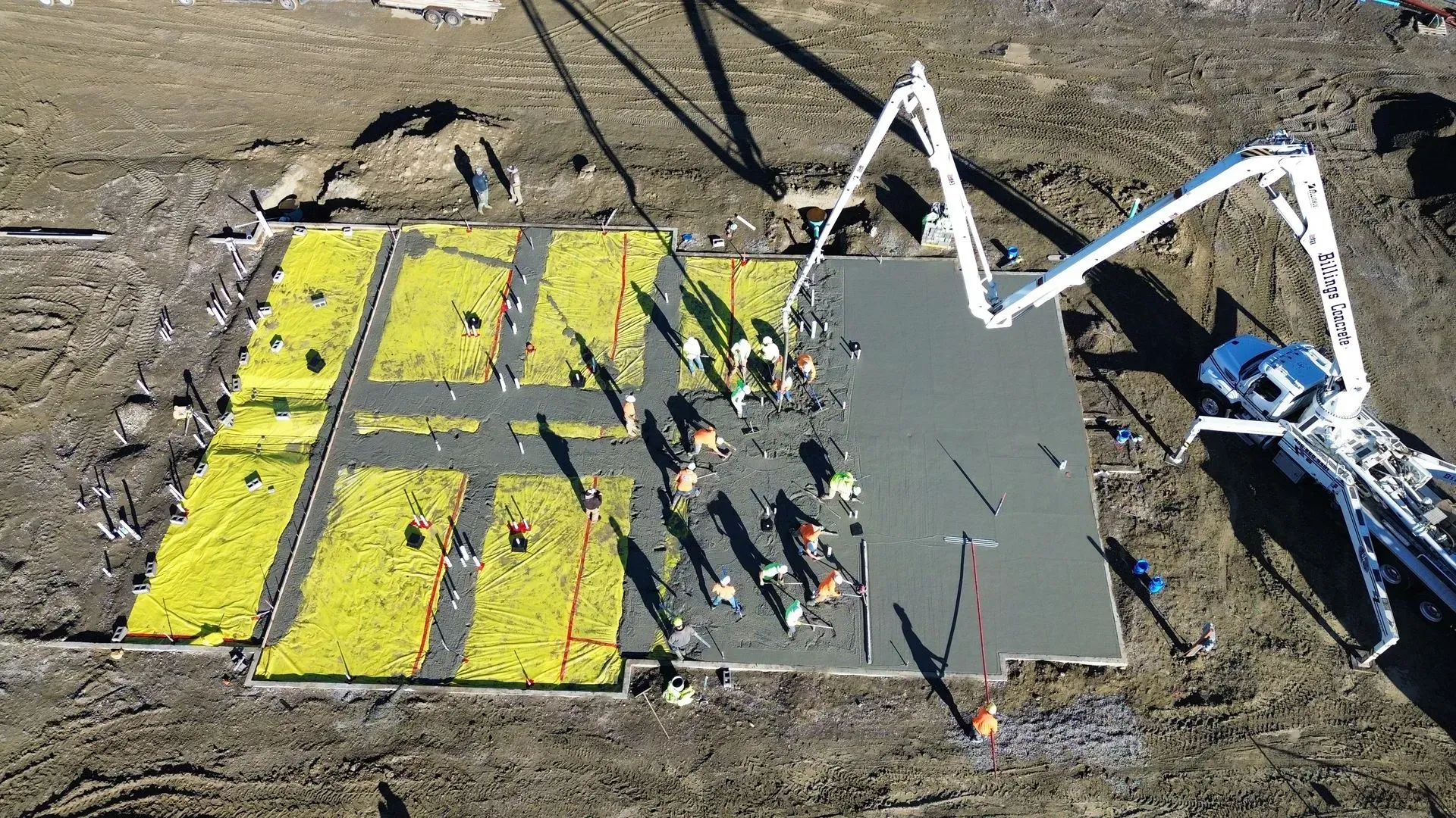 Large painted square with gray and yellow panels and a white excavator arm beside it on a dirt site