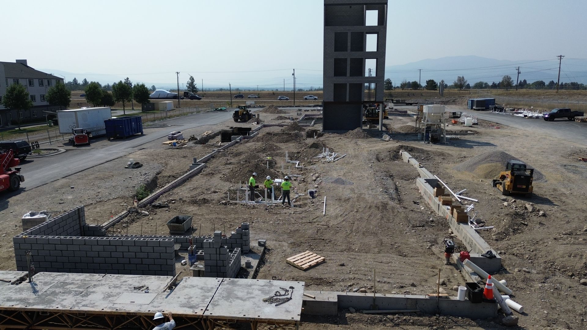 Construction site with a tall unfinished concrete building and workers amid earthworks and debris
