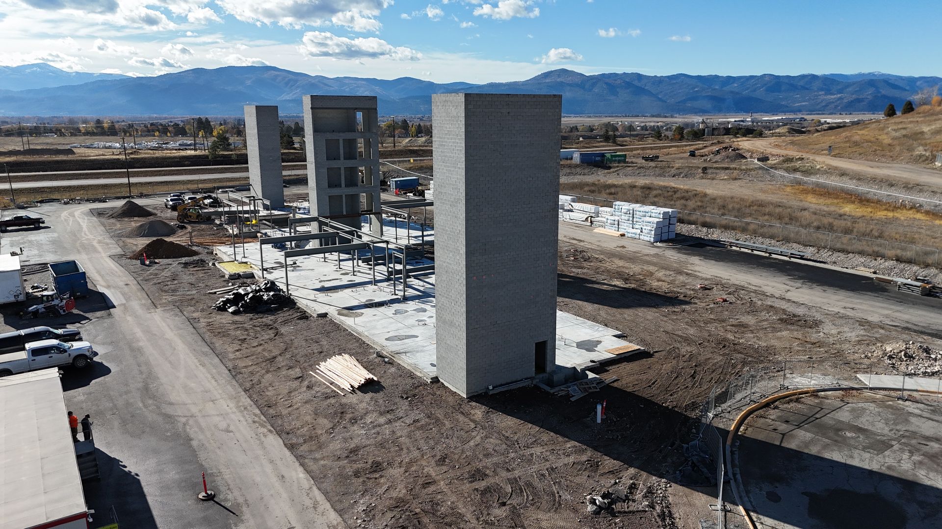 Construction site with tall concrete towers and cranes under a clear sky, mountains in the background