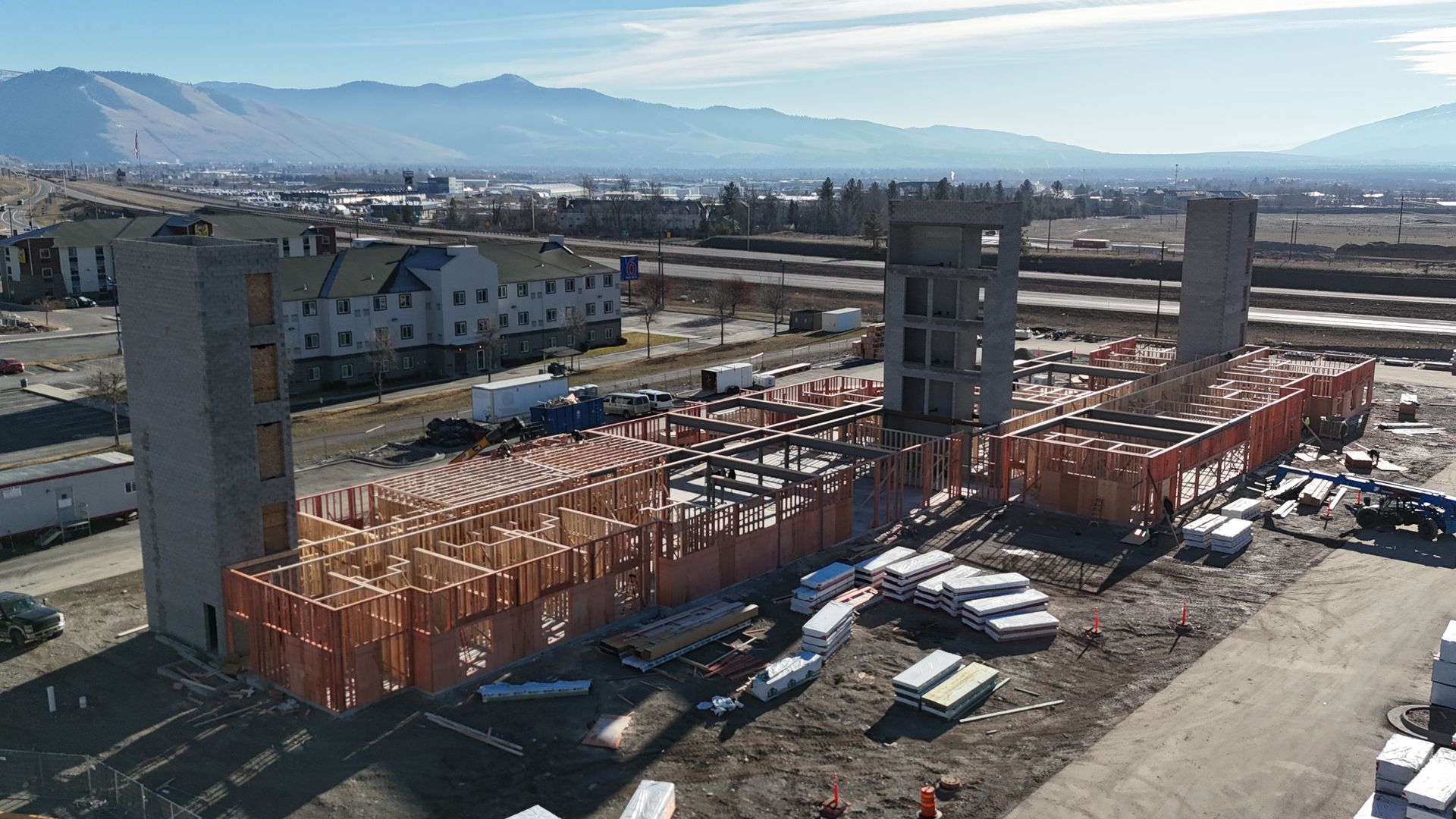 Construction site with a steel building frame under assembly in an open lot, mountains in the background
